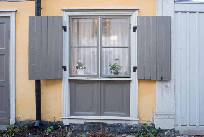 Fönster mot Breda gatan med luckor och dekorativt ramverk under. Foto: J. Malmberg. gul kulör, gröna luckor och bruna lister.