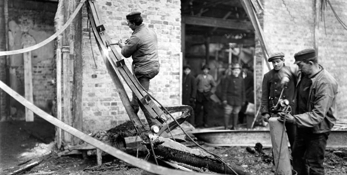 BRANDKONTORET Ovan. Svetsarbete för återuppbyggnad efter brand i maskinverkstaden hos AGA Lidingö, 1915. Ur AGA:s arkiv hos Centrum för Näringslivshistoria.