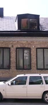 Husetss fasad har grågult tegel, med en gråmålad