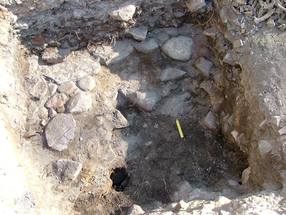 lager 2. Ungefär 0,85 m under dagens markyta påträffades en stenläggning av både kalk- och gråsten. Stenläggningen utgör sannolikt en del av en gårdsläggning. Foto över ruta 2 från söder.