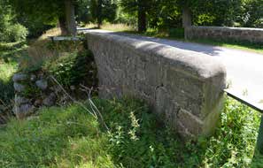 12-1158-1 Bro över bäck vid Övedskloster västra bron) Bron från 1761 har en udda och kompakt form där det lilla rundbågevalvet nästan göms under den höga övermurningen och de grova stödmurarna vid
