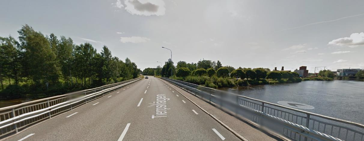 Figur 3. Den aktuella kraftledningen sedd från bron över Garvarforsen. Ledningen döljs i huvudsak av vegetation längs älvstranden. Industriområdet syns till höger i bild. Foto från GoogleMaps.