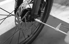Ta fram den genomgående axeln för framhjulet ur Tool Kt. Sätt hjulet gaffeln och för samtdgt n bromsskvan bromsoket.