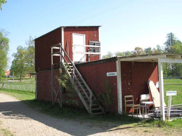 Dörrar En modern trädörr med vertikal panelning med sparkplåt nedtill, svartmålad. Betongtrappa finns här med två sättsteg. En enklare svart bräddörr med horisontella brädor.