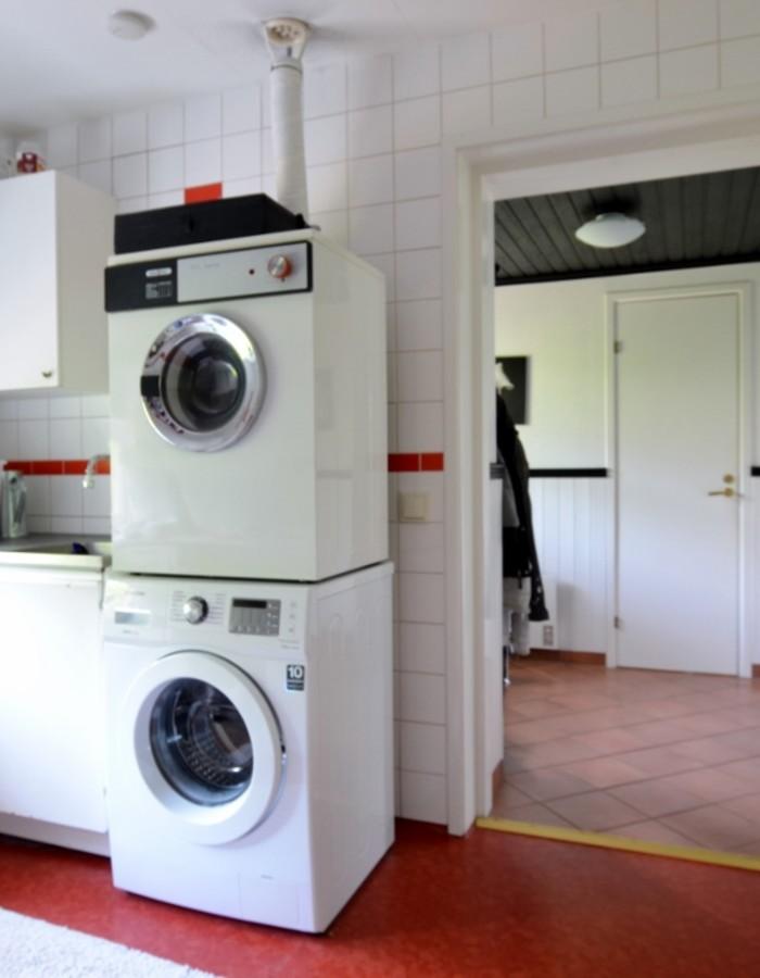 Tvättstuga Tvättmaskin (2013) och torktumlare i stapel. Vit inredning och vask.