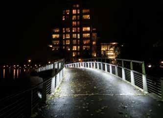 Det är kontrasten mot KCCC:s varmvita ljus som gör bron nästan blå på långt håll. Foto: Frida Almqvist. Naturfärgad lekutrustning kan kvällstid färgas in med ljus. Ljusdesign: Tyréns.