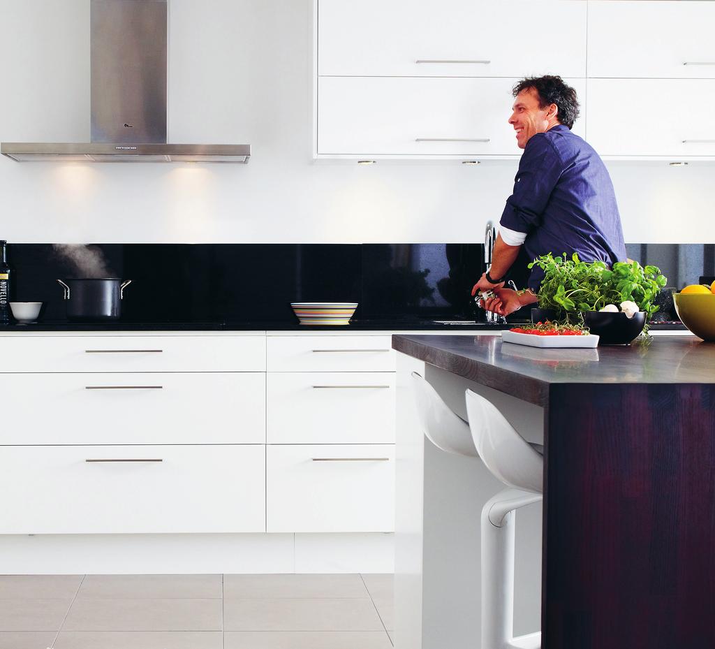 Kök. Köket har vitvaror i rostfritt stål, stänkskydd i vitt kakel, mörkgrå bänkskivor och en frihängande fläktkåpa.