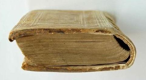 Om boken eller arkivmaterialet förvaras i olämplig miljö, kan felaktig hantering leda till än större skador. Två böcker som deformerats på grund av felaktig placering i hylla. Foto: Victoria Juhlin.