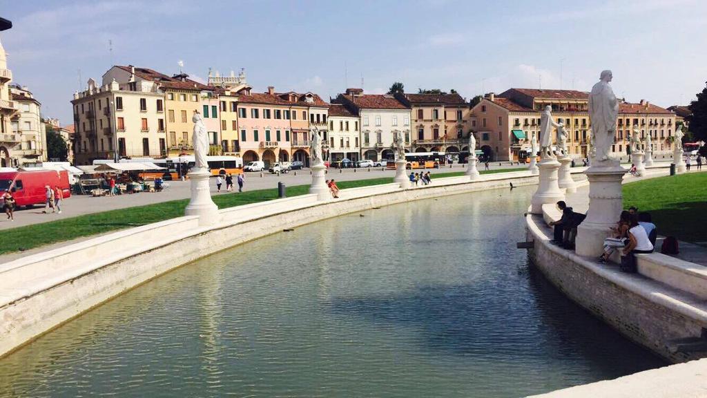 En bild från ett soligt Prato della valle Padovas mittpunkt. En park omringad av vatten och statyer av män som gjort något stort för staden.