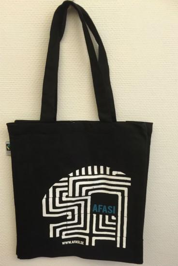 T-shirts och tygkassor designat av Mathilda Cederlund, Både t-shirt och tygkasse är svart med vit labyrint och turkosblå, text med ordet afasi tryckt på.