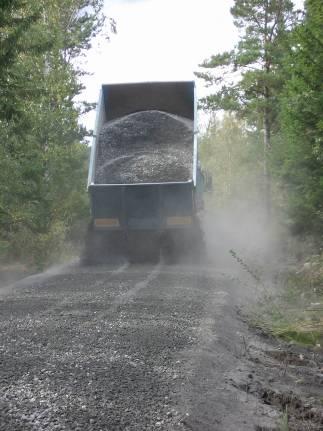 Stackarna med flygaska jämnades av över vägytan med grävmaskin, figur 10a. Med väghyvel jämnades flygaskan ut sedan i ca 0,2 m skikt.