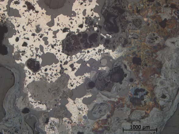 Figur 29. F1127 fotograferad i mikroskopet på etsat prov. De släta grå ytorna är finkornig slagg. De flammiga grå ytorna är rost. Den ljusa delen är kolfritt järn (ferritiskt).
