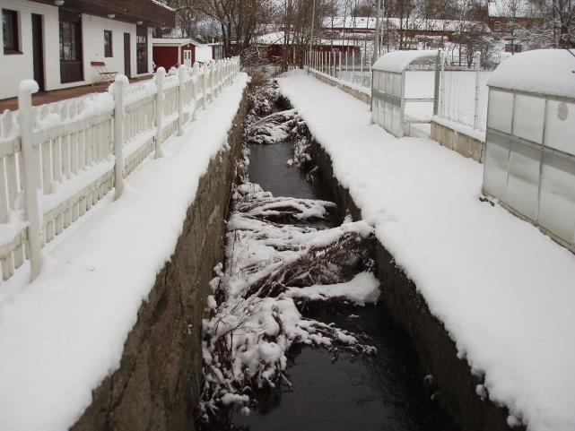 Trydeån som passerar idrottsplatsen och friluftsbadet. Längs med bäcken finns en smal passage som är för liten för att allmänheten ska kunna ta sig genom passagen obehindrat.