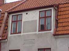 Murad utbyggnad och veranda åt söder. Delvis inbyggd balkong över med räcke av röd korrugerad plåt och tak av korrugerad plast.