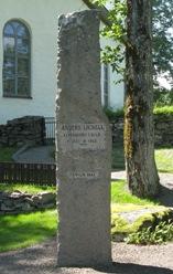 Över porten finns inskriptionen: "Axel F. Johansons Familjegrav". Plåttäckt tälttak som kröns av en fackellåga i metall.