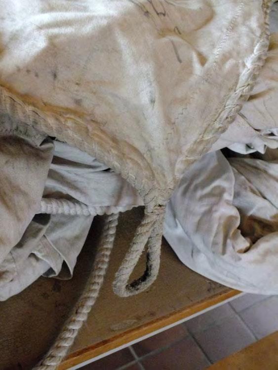 Till vänster, detalj av befintliga segel. Notera hur repet har sytts fast för hand i segelduken (segelliket). Till höger att andelbevis som föreningen sålt för att få in pengar till verksamheten.