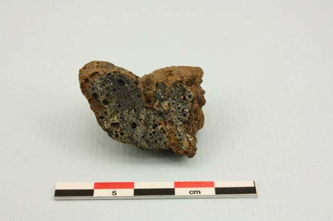 Fragmentet tolkat som smält lera sågades. I tvärsnitt ses en heterogen slagg med inslag av smält lera/sand (fig 5). Enstaka större mineralkorn förekommer. Inget träkol kunde observeras i tvärsnittet.