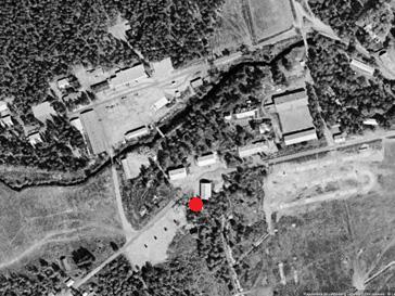 Figur 3. Från Eniros historiska flygfoton, fotat på 1950-talet. I fotot framgår tydligt de områden med hårdgjorda ytor. Den röda punkten markerar platsen som var föremål för förundersökningen.