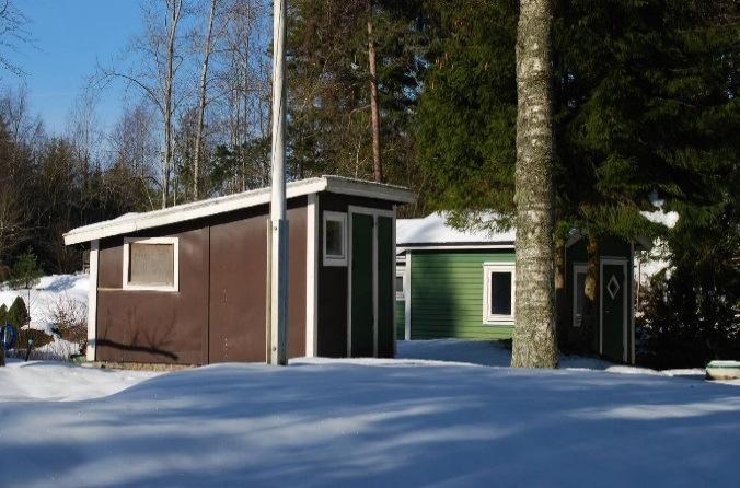 Bostadsbyggnaden har skärmtak och entré på gaveln samt liggande brunmålad träpanel.