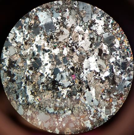 Figur 9: foto på tunnslip av melanokratisk granit. Notera de omvandlade plagioklaskornen. Kalifältspatskornen är cirka 1mm. Fotot är taget i xpl.