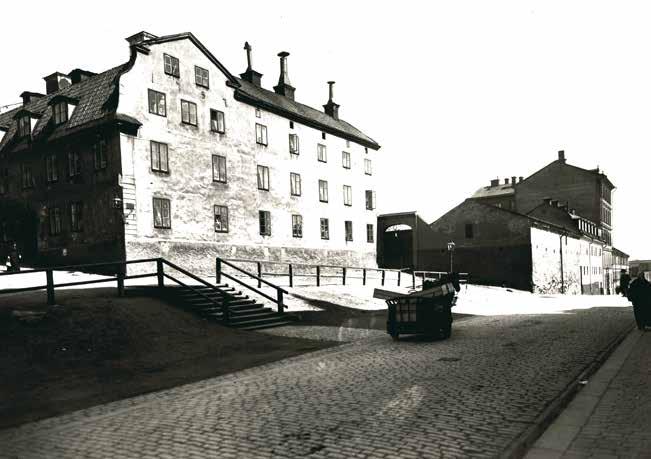 DROTTNINGEN 5 I BÖRJAN AV 1900-TALET. BOSTADSHUSET TILL VÄNSTER OCH DET LÅGA MAGASINET MED SINA SÄRPRÄGLADE MURAR TILL HÖGER. FOTO LARSSONS ATELJÉ, SSM C126.