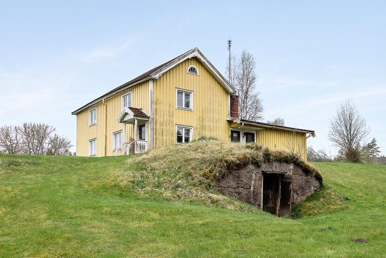 Ytterfasad av gulmålad träpanel och vita detaljer under tak med betongpannor.