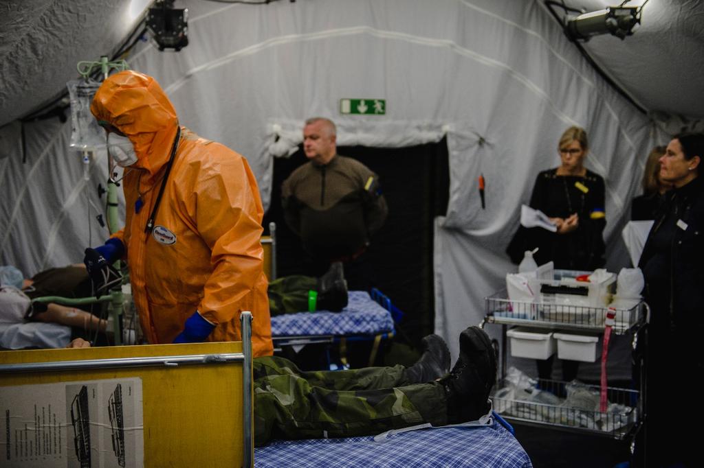 Observatörer på plats i fältsjukhusets vårdsal medan sköterska i PPE tar hand om de (i övningsscenariot) insjuknade hemvärnssoldaterna. Foto Astrid Amtén Skage/Försvarsmakten 4.