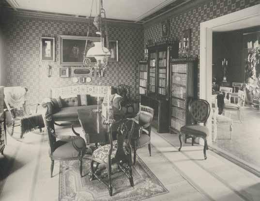 SYSSLOMANNENS BOSTAD PÅ VÅNING 1 TRAPPA I VALENTIN- HUSET 1896. RUM- MEN ÄR INREDDA PÅ TIDSTYPISKT VIS MED DOVA, MÖNST- RADE TAPETER OCH MÖRKA MÖBLER.