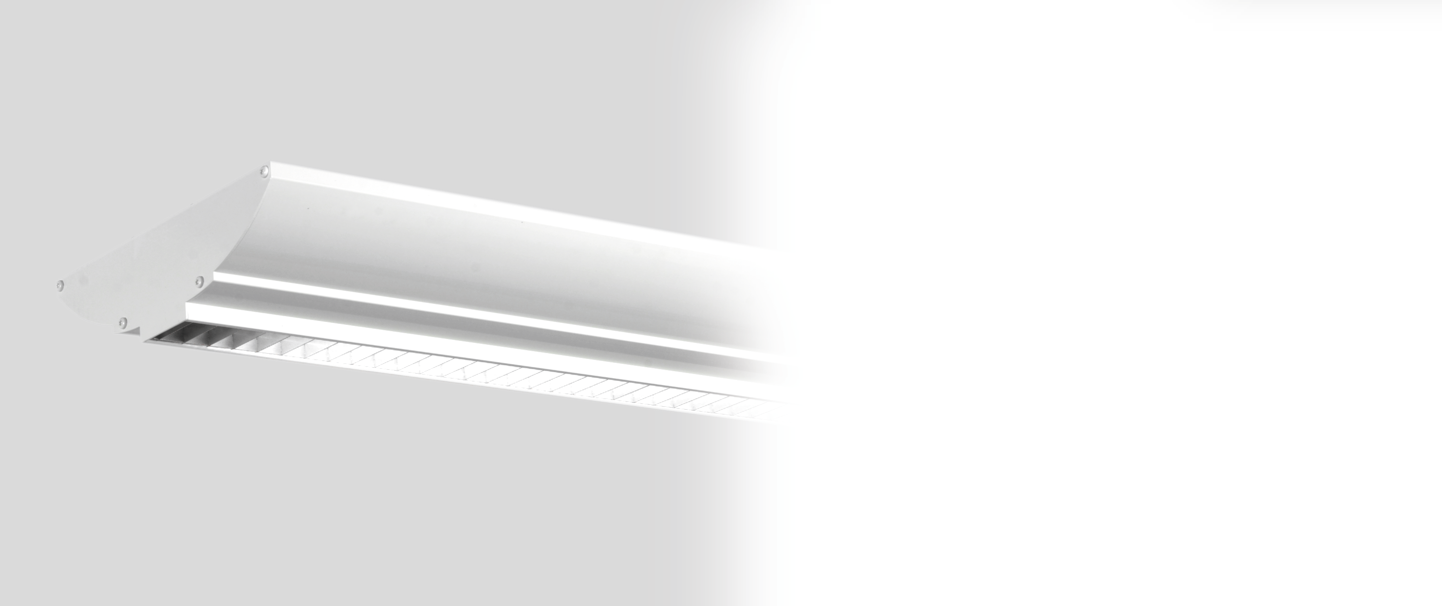 INTERIÖR TRIOLUX 0 Pendlad armatur av strängsprutad alumnium med plåtgavlar, vitlackerad. Silvergrått tvärlamellbländskydd. Reflektorer för såväl nedljus som uppljus.
