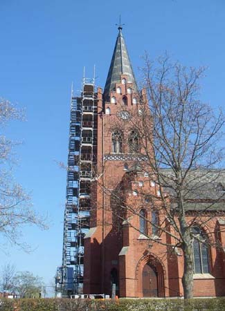 T.v. Tygelsjö kyrkas västra tornfasad under renovering. T.h. Tinnarna på tornets västra gavelparti med omfattande fogsläpp och kalvande murverk, sett från söder.