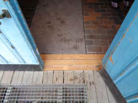 Vid entrén till Naturporten finns en dörröppnare på väggen bredvid dörren (bild 6). Den sitter dåligt till för att en person i rullstol ska kunna nå den från rampen.