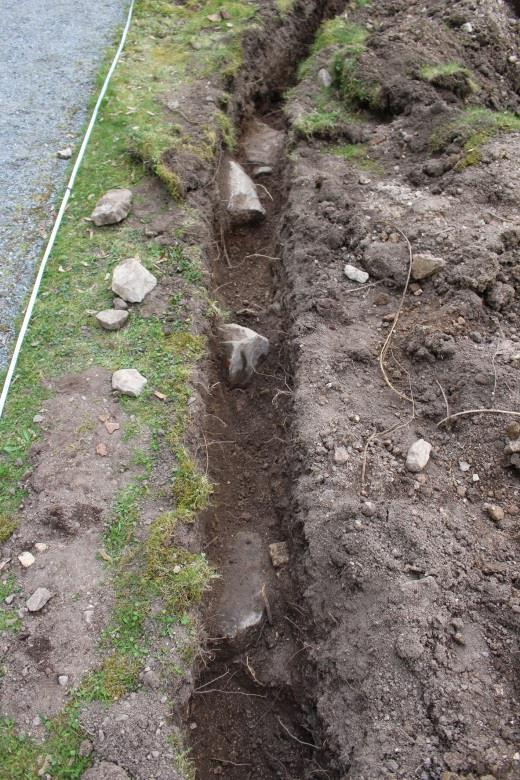 C Stenmur. Längs kyrkans norra sida påträffades resterna av en stenmur ca 1,4 m väst om B (figur 7 och 9). Murresterna låg ca 0,15 0,3 m under mark och låg tillsynes i nord-sydlig riktning.