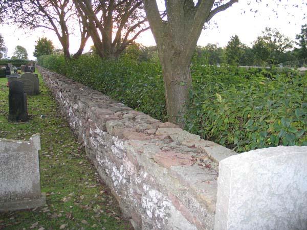 (KI Böda kyrkog 004) Gränsen mellan kvarter G och den del av kyrkogården som tillkom på 1990 markeras av den gamla kyrkogårdsmuren, syrenhäck och en rad av oxlar och lönnar.