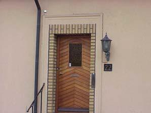 Brunlaserad lamelldörr med panel i fiskbensmönster och råglasruta. Profilerad dörromfattning, gult tegel runt dörröppning.