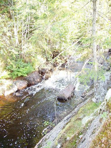 Dammen utgör en kulturmiljö. Vattnet styrs till en sprängd kanal med hjälp av rensade stenblock som blockerar naturfåran (foto 11 & 12).
