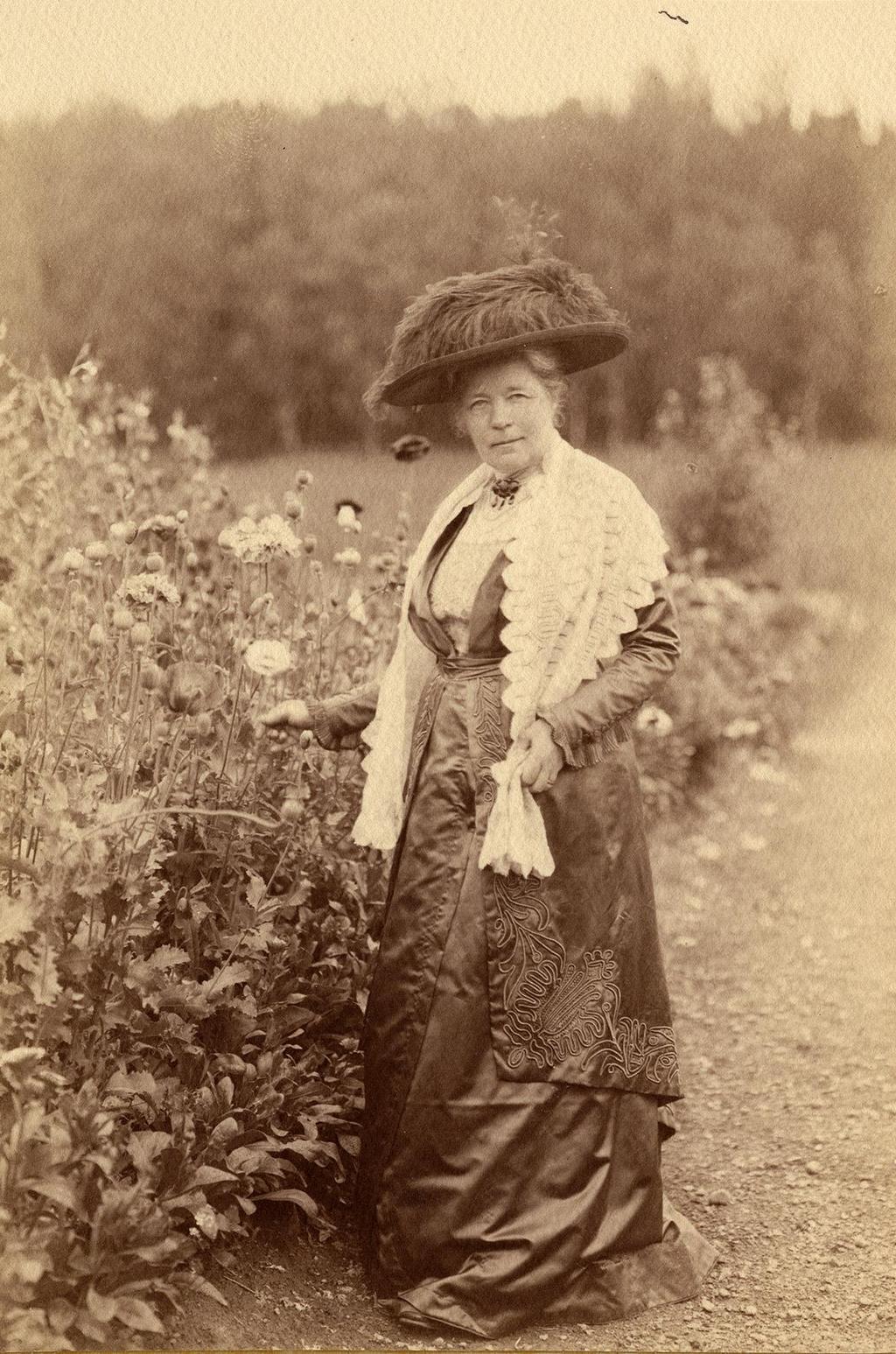 Selma Lagerlöf i köksträdgården omkring 1913 med handen i en rad av pionvallmo.