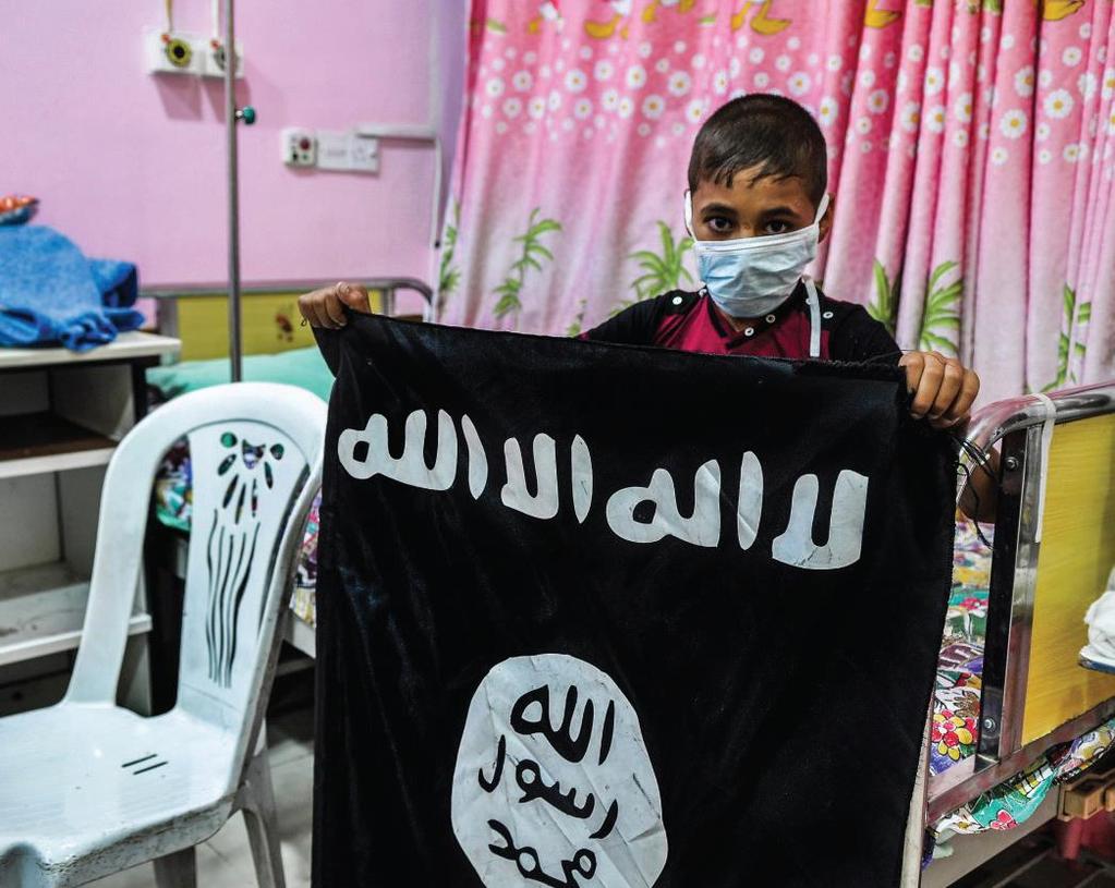 Bild 6.2. Dabiq nummer 4 sid 28. Ett barn som sägs få cancerbehandling på ett IS-kontrollerat sjukhus visar upp the flag of Tawhid flaggan som är en symbol för IS.