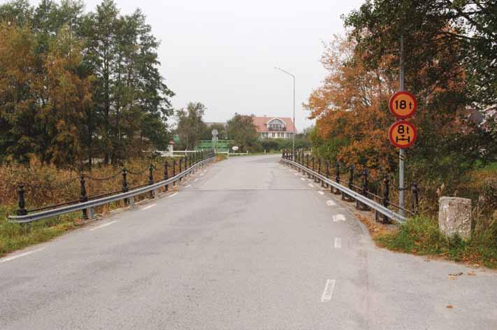 Gjutjärnsstolparna i räckena och påbudsskylten om nedsatt bärighet varslar om att bron vid Norje är gammal. Bärverket är lågbyggt och brobanan ligger i nivå med omgivningarna.