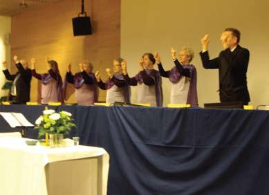 Kören, bestående av fem damer i ljuslila blusar med mörklila tyg draperat över axlarna och två män i mörk kostym tecknade psalmen Hosianna.
