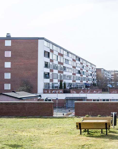 Ett långt led av förskolebarn med gula västar går förbi fotbollsplanen av grus bakom Bäckgårdsvägen i Vårby gård.