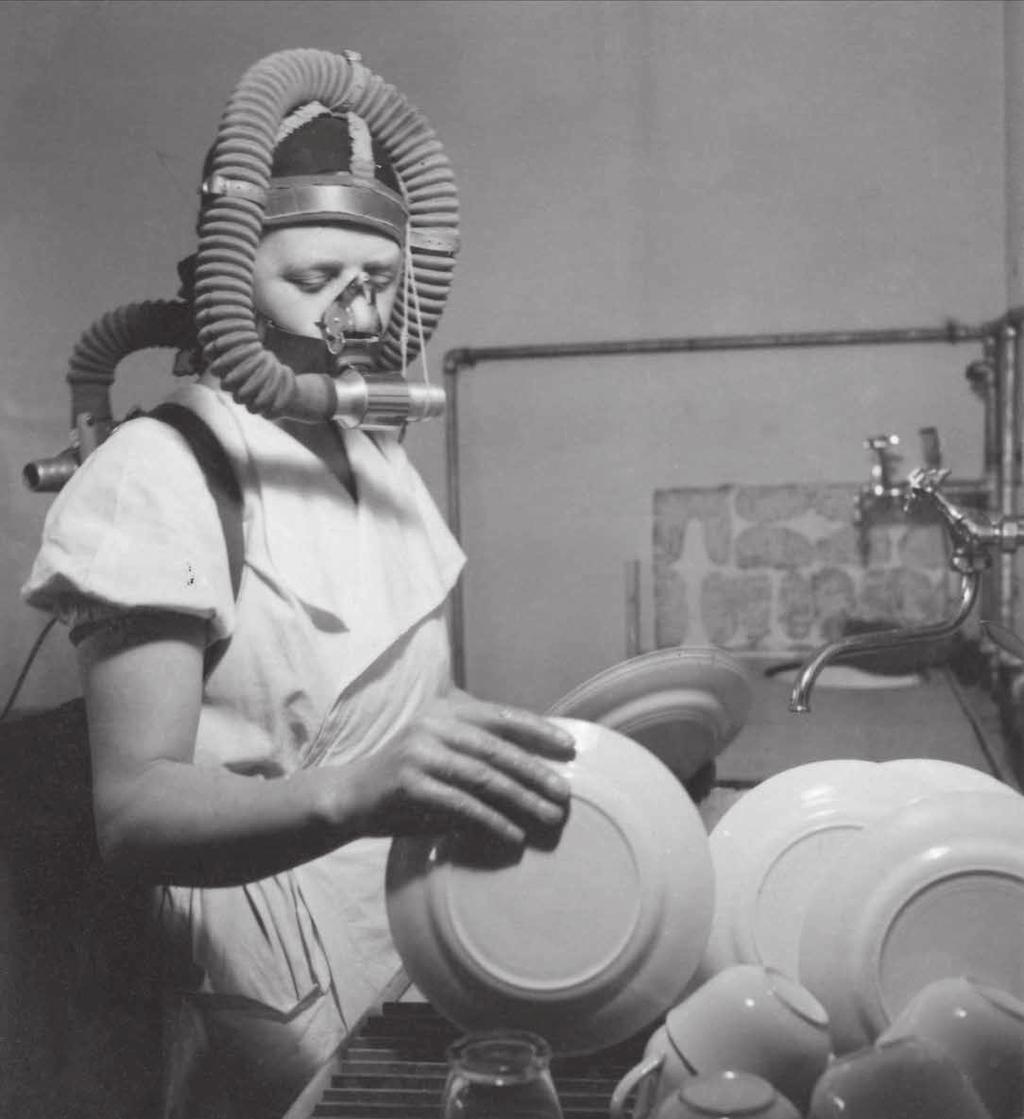 Kvinna i syrgasmask diskar i kök, 1944. Hemmens forskningsinstitut (HFI) hade som syfte att rationalisera hem- och hushållsarbete.