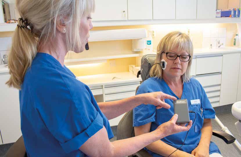 Marie Karlsson visar hur muskelaktivitetsmätaren, biofeedback, mäter aktiviteten i ansiktets muskler och i tungan med hjälp av en sensorplatta på patientens kind.