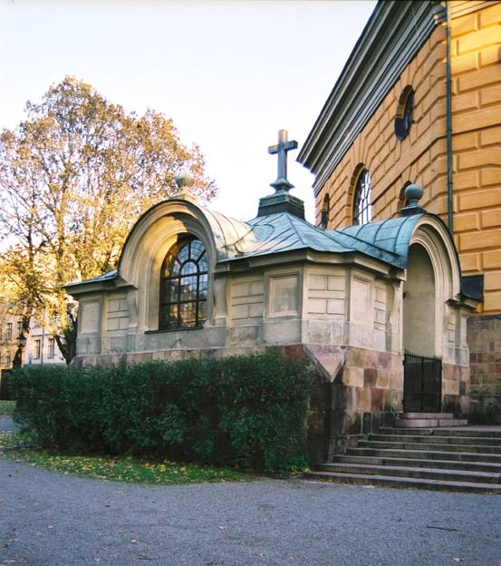 Dörrarna av trä är brunmålade, indelade i speglar med snidad dekor. Till porten i väster leder en dubbeltrappa.
