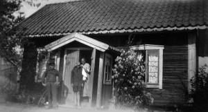 Minas stuga upp i Fors By, hon står själv i dörren,.flickan kan vara någon av döttrarna.
