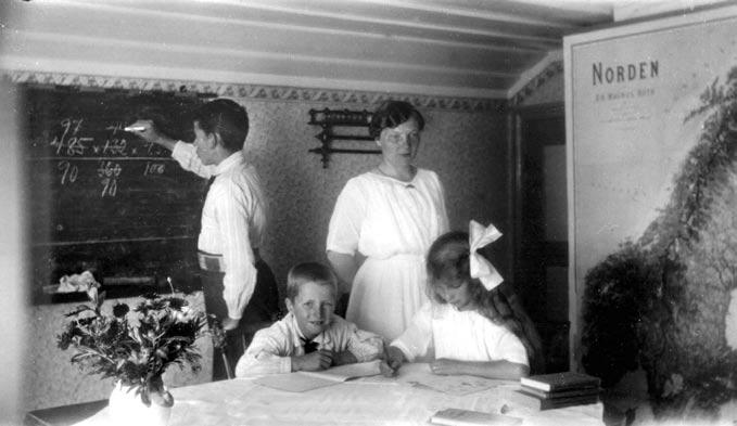 Examen vid lotsbarnskolan. Bilden är från år 1922 och från Pater Noster fyrplats med Adriana Olsson som lärare. Man är uppklädda i finkläder. Lägg märke till blommorna på bordet.