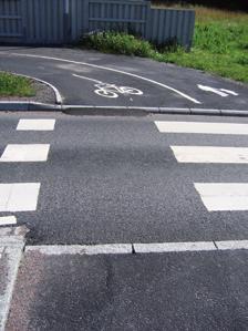 Utformning 25 3:23 Cyklister åker på övergångsstället Beläggning Normal standard på cykelbanorna är svart asfalt. På speciella platser kan annan beläggning vara önskvärd av estetiska skäl.