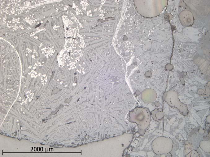 I mikroskala framträder en komplext uppbyggd slagg med varierande mineralinnehåll och förekomst av magnetit (ljusa långsmala band).