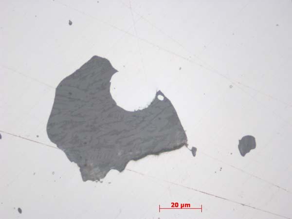 Slaggen består av wüstit (ljus), olivin (ljust grå) och en glasfas (mörkare grå). Se analysområde 1a-c i tabell 1). Foto från mikroskopet. Skala i nedre kanten. Oetsat prov. Figur 6.