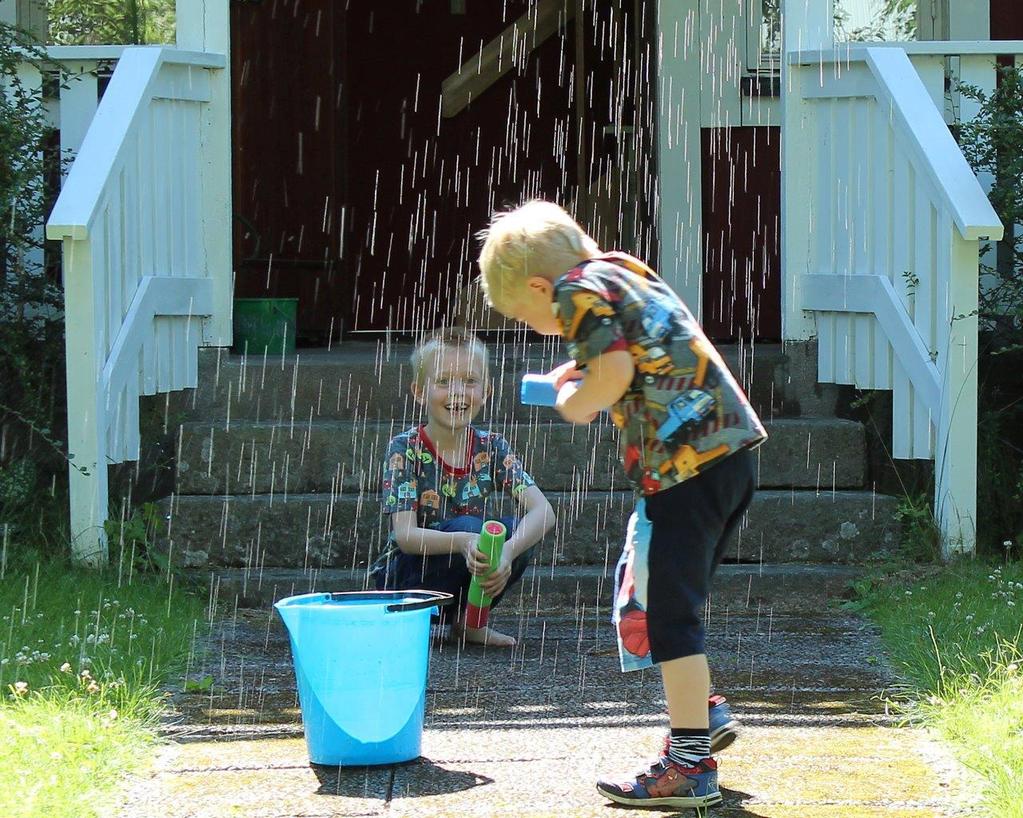 10. Gunilla Fagerkvist Ursjö Två pojkar leker i solen. Det är sommar, gräset är grönt och oklippt. Byggnaden i bakgrunden har en känsla av sommarstuga över sig sig. Klöver sticker upp ur gräsmattan.