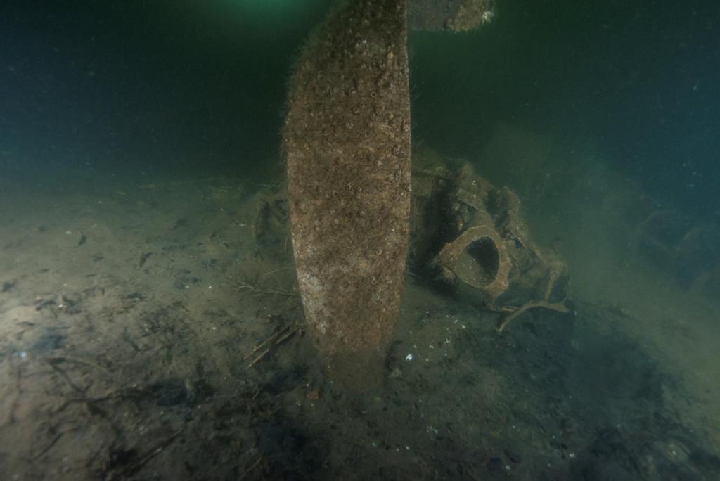 6 Propeller och motorns luftintag. Foto: Ingemar Lundgren, Ocean Discovery. 7 Propeller och motor. Foto: Ingemar Lundgren, Ocean Discovery. Havsbotten på platsen består av lös, lättflyktig och mörk sediment i vilket delar av flygplanet är delvis nedsjunkna.